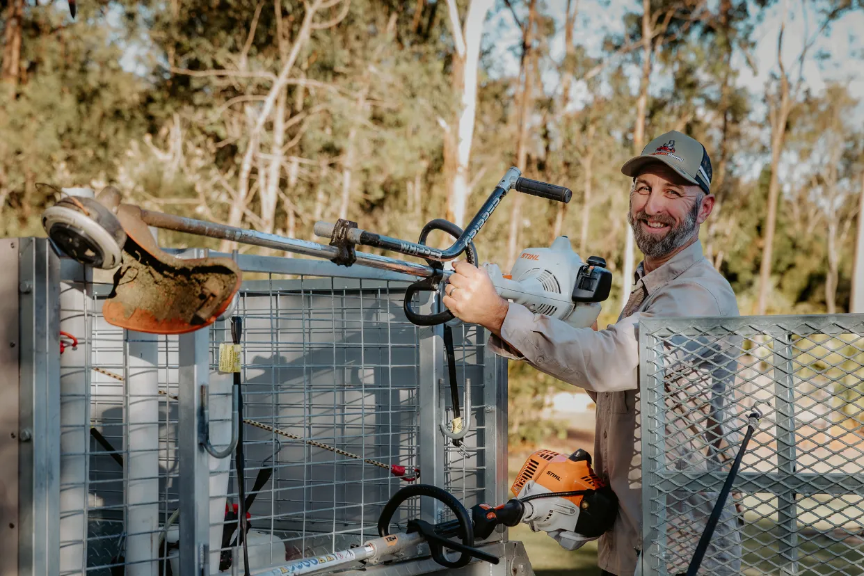Smiling man loading his whipper snipper onto his work trailer.